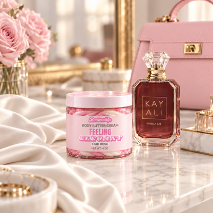 Butterwhip Feeling Elegant Oud Rose Body Butter Cream on a marble vanity beside Kayali Vanilla 28 perfume, a pink handbag, ivory satin, and pink roses.